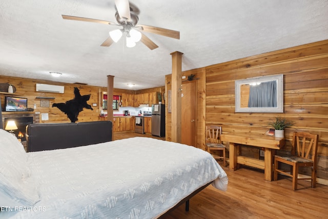 bedroom with wooden walls, a textured ceiling, a wall mounted AC, light hardwood / wood-style floors, and stainless steel refrigerator