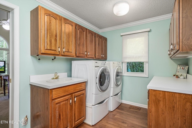 laundry room featuring cabinets, ornamental molding, a textured ceiling, sink, and washing machine and clothes dryer