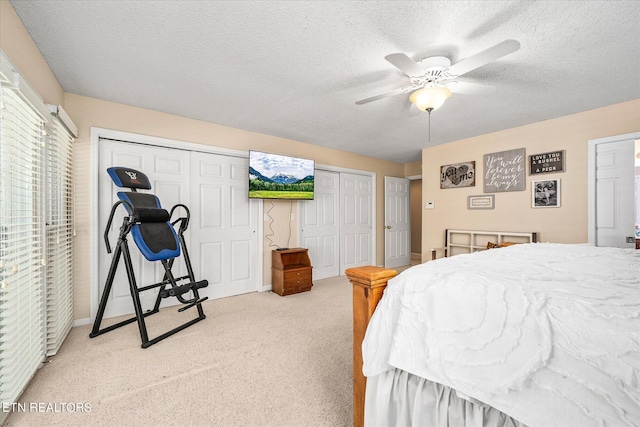 bedroom featuring a textured ceiling, ceiling fan, light carpet, and multiple closets