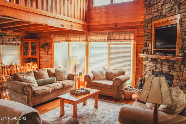 living room with a towering ceiling, a stone fireplace, and light wood-type flooring