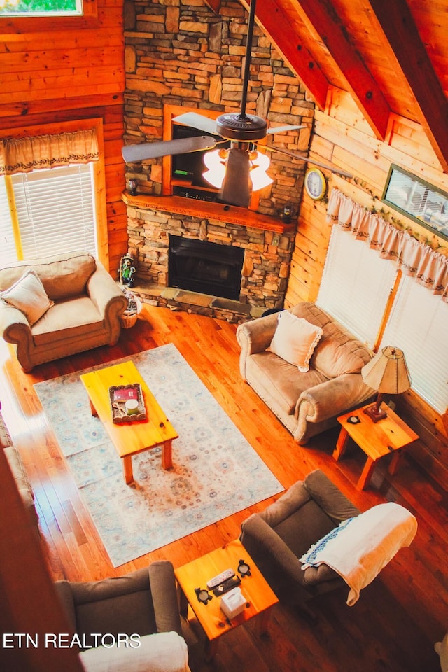 living room featuring wood walls, beam ceiling, wood-type flooring, a stone fireplace, and high vaulted ceiling