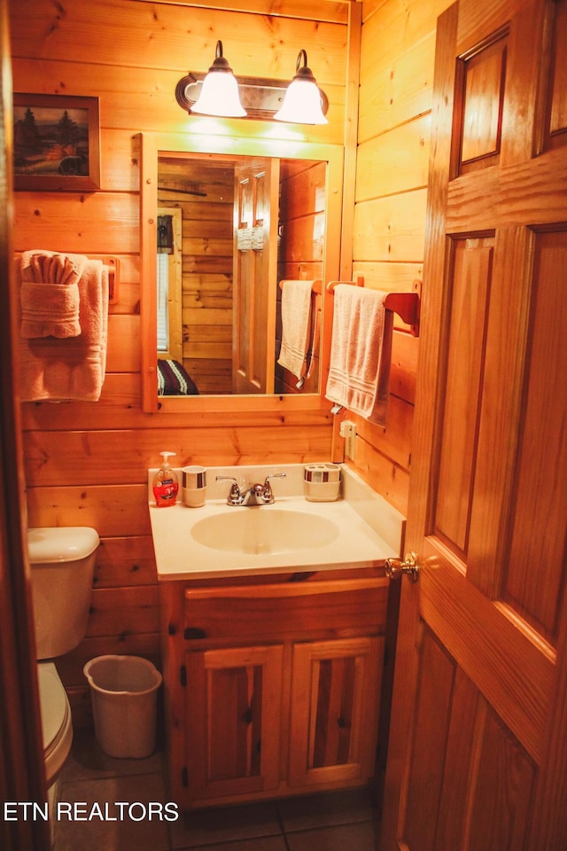 bathroom with tile patterned floors, toilet, vanity, and wooden walls