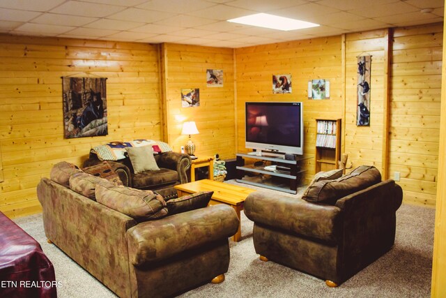 living room with carpet floors, a paneled ceiling, and wooden walls