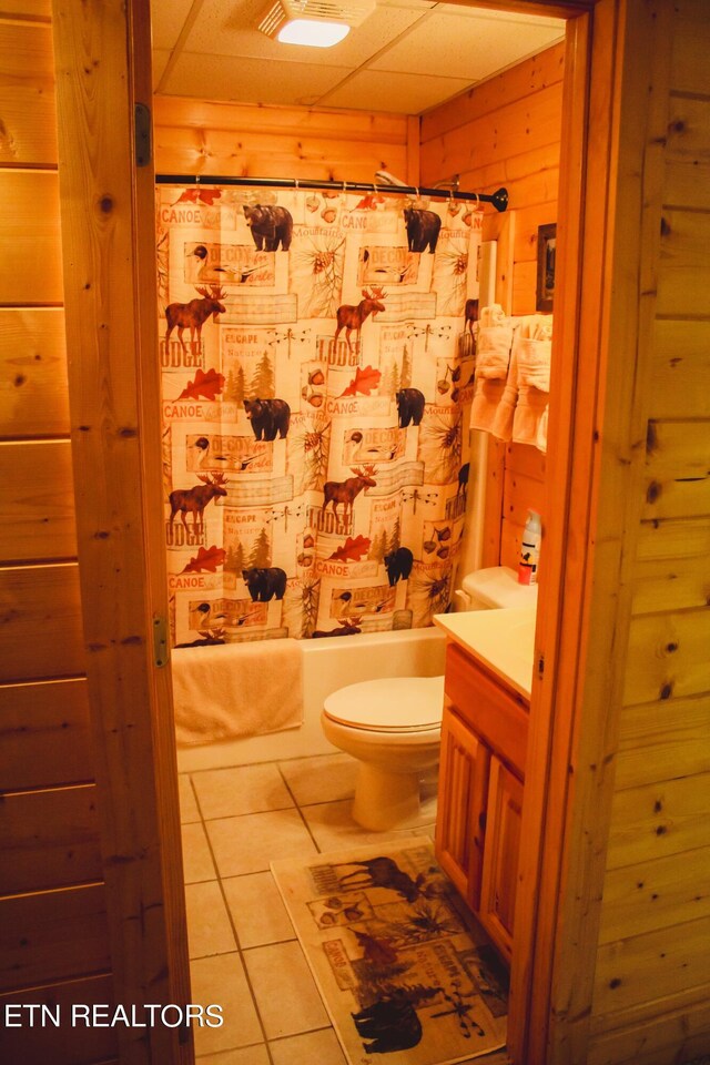 full bathroom with toilet, wooden walls, shower / bathtub combination with curtain, tile patterned floors, and vanity