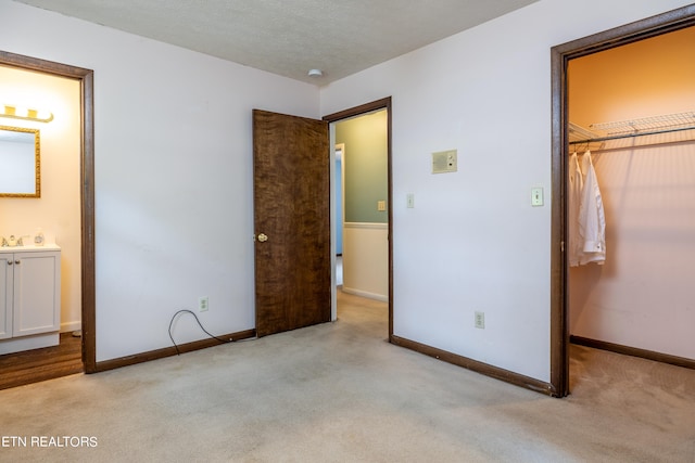 unfurnished bedroom with sink, a closet, a spacious closet, ensuite bathroom, and light carpet