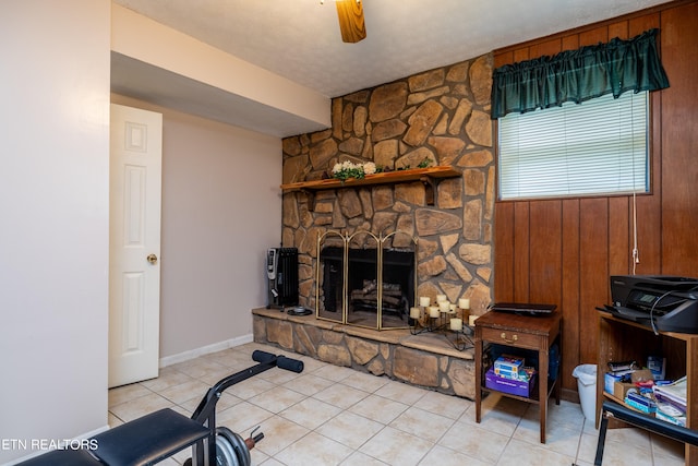 tiled living room with ceiling fan, wooden walls, and a stone fireplace