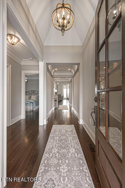 entryway with vaulted ceiling, dark hardwood / wood-style floors, crown molding, and an inviting chandelier