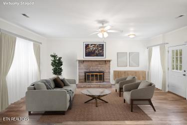 living room featuring ceiling fan, crown molding, light hardwood / wood-style flooring, and a brick fireplace