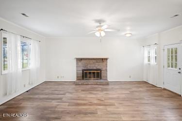 unfurnished living room with a brick fireplace, hardwood / wood-style flooring, ornamental molding, and ceiling fan