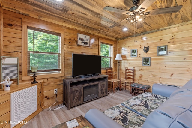 living room featuring ceiling fan, light wood-type flooring, wood ceiling, and wooden walls