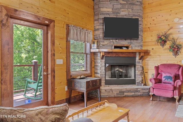 living room with wood-type flooring, a stone fireplace, and wood walls