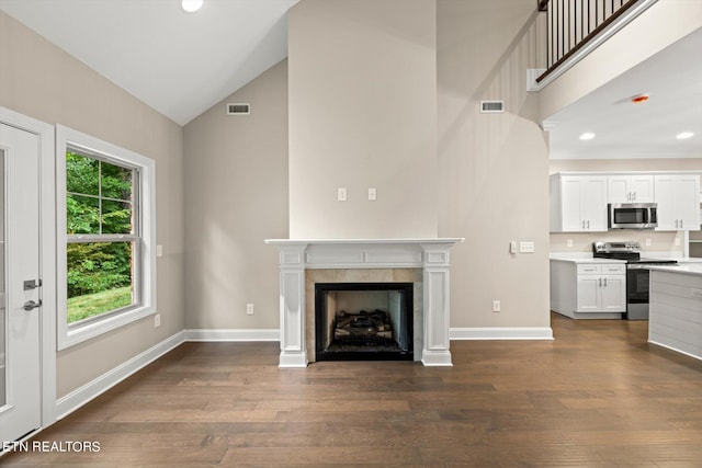 unfurnished living room with high vaulted ceiling, a tile fireplace, and dark hardwood / wood-style flooring