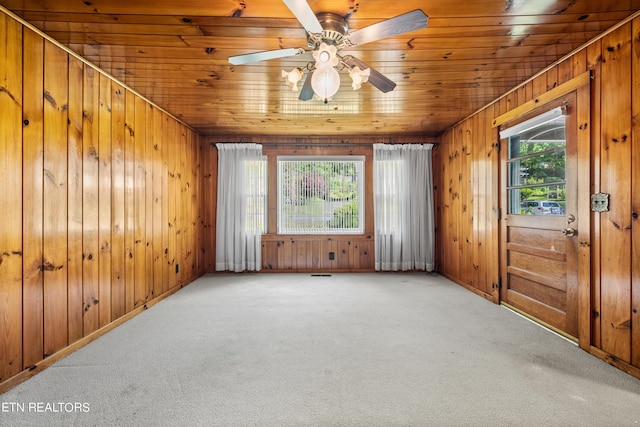 spare room featuring carpet flooring, plenty of natural light, wooden walls, and ceiling fan