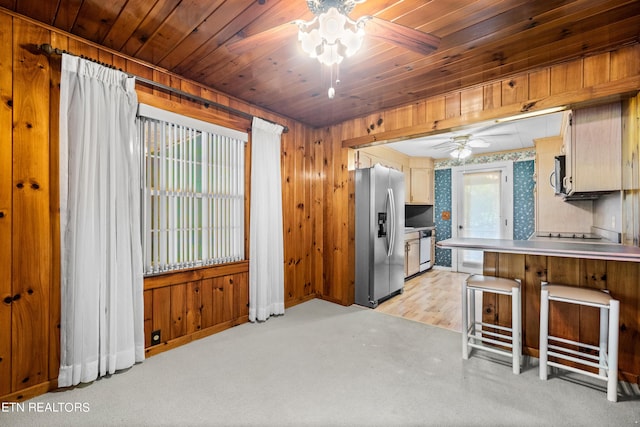 kitchen featuring wood walls, a kitchen breakfast bar, ceiling fan, stainless steel fridge, and light colored carpet