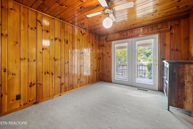 carpeted spare room featuring wood walls, ceiling fan, and wood ceiling