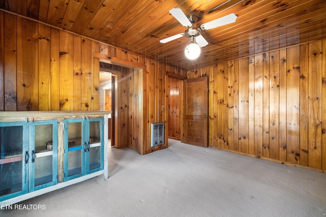 carpeted spare room with ceiling fan, wood walls, and heating unit