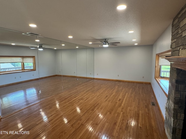 empty room with a textured ceiling, hardwood / wood-style flooring, a stone fireplace, and ceiling fan