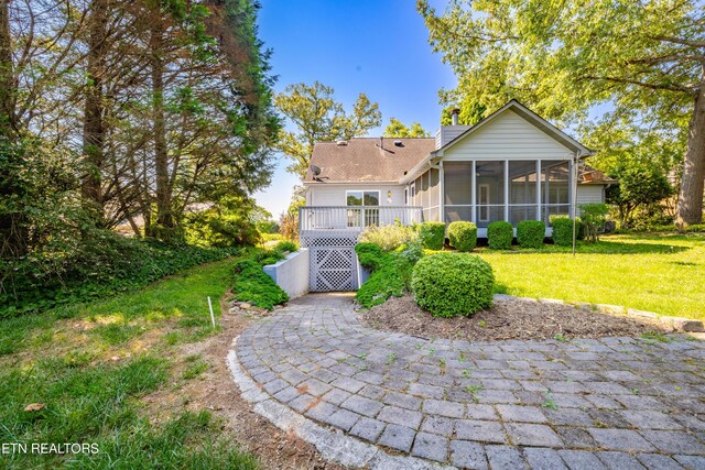 rear view of house with a sunroom, a deck, and a lawn