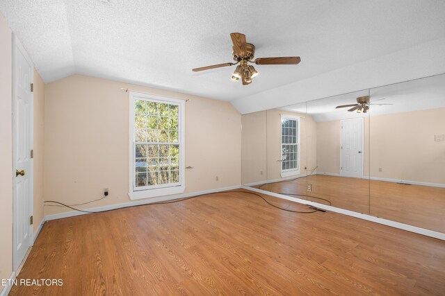 empty room with ceiling fan, lofted ceiling, a textured ceiling, and light hardwood / wood-style flooring