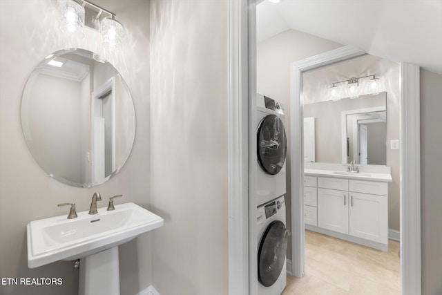 bathroom with dual sinks, stacked washer / dryer, tile patterned floors, and vaulted ceiling