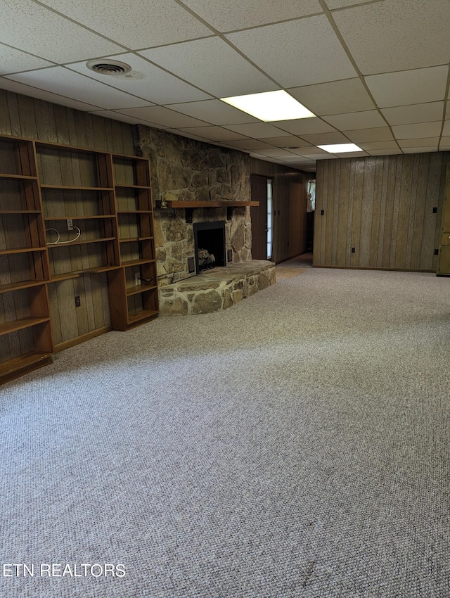 basement featuring a fireplace, a paneled ceiling, carpet floors, and wooden walls