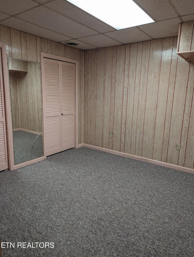 basement with carpet flooring, a drop ceiling, and wooden walls