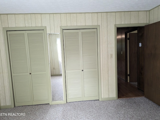 unfurnished bedroom featuring carpet, multiple closets, and wooden walls