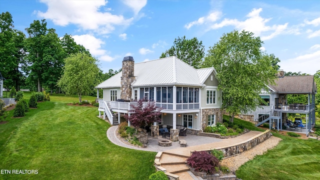 rear view of property featuring a patio area, a sunroom, a yard, and an outdoor fire pit