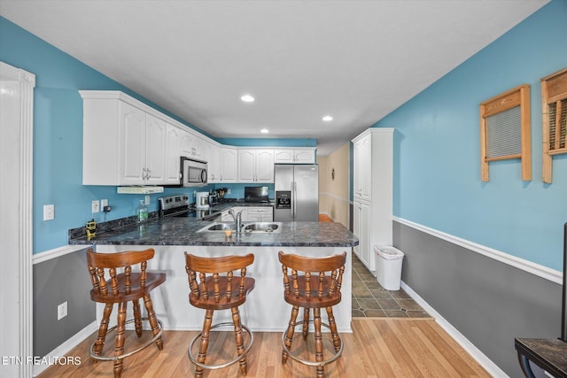 kitchen featuring kitchen peninsula, a kitchen bar, sink, appliances with stainless steel finishes, and white cabinets