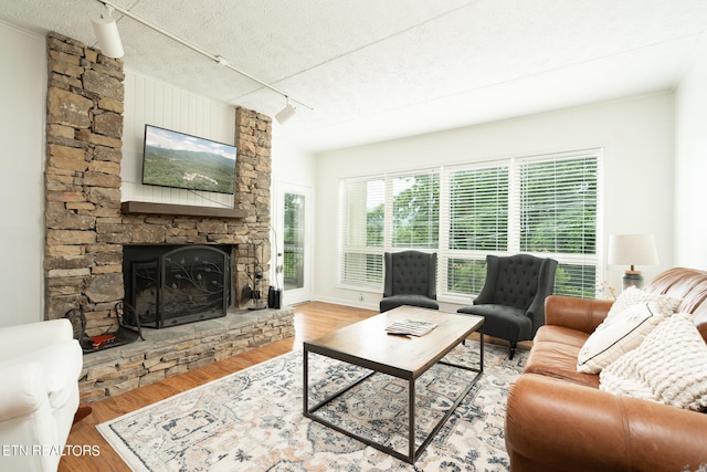 living room with a textured ceiling, light hardwood / wood-style floors, a stone fireplace, and track lighting