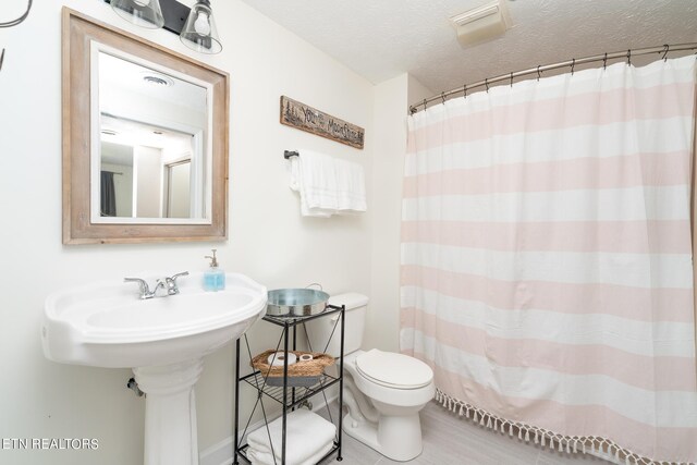 bathroom with toilet, a textured ceiling, and tile patterned floors