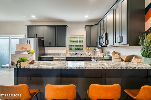 kitchen with stainless steel appliances, sink, light stone countertops, and kitchen peninsula