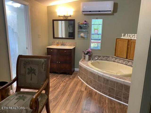 bathroom with tiled bath, vanity, hardwood / wood-style flooring, and an AC wall unit