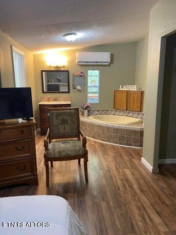 bedroom with a wall unit AC, a textured ceiling, and hardwood / wood-style flooring