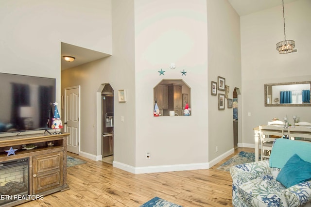 living room featuring light wood-type flooring, an inviting chandelier, and a high ceiling