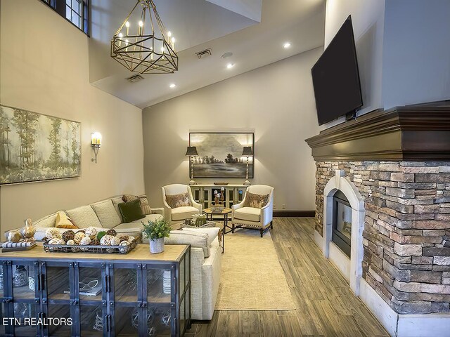 living room featuring hardwood / wood-style flooring, high vaulted ceiling, a notable chandelier, and a fireplace