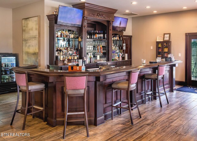 bar featuring hardwood / wood-style floors, wine cooler, and dark brown cabinetry