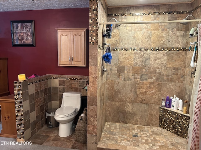 bathroom featuring a textured ceiling, toilet, a tile shower, and tile walls