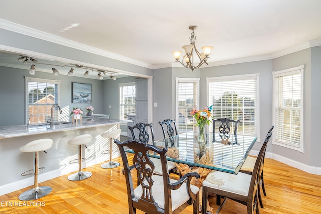 dining area with crown molding, sink, light wood-type flooring, and a chandelier