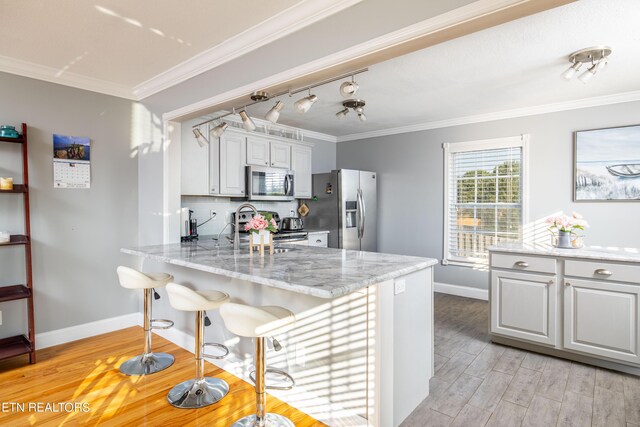 kitchen featuring white cabinets, stainless steel appliances, ornamental molding, and light hardwood / wood-style flooring