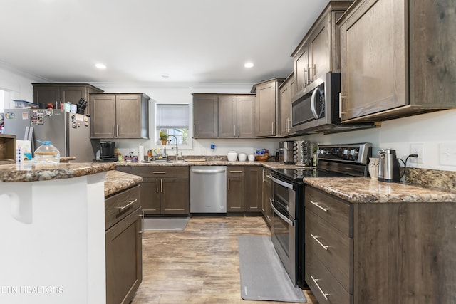 kitchen featuring dark brown cabinetry, stainless steel appliances, light hardwood / wood-style flooring, and crown molding