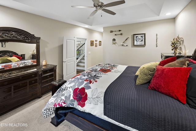 bedroom with ceiling fan, light colored carpet, and a raised ceiling