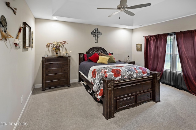 carpeted bedroom featuring ceiling fan and a raised ceiling