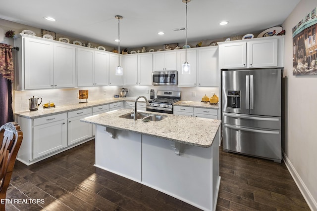 kitchen with pendant lighting, white cabinets, stainless steel appliances, sink, and a kitchen island with sink