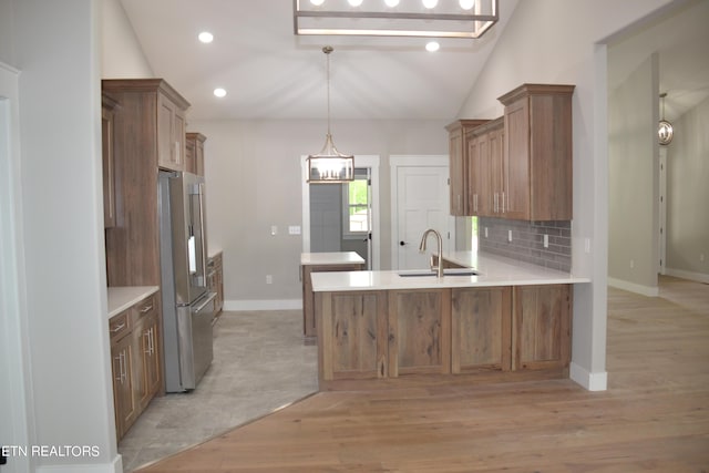 kitchen with kitchen peninsula, light wood-type flooring, high quality fridge, sink, and lofted ceiling