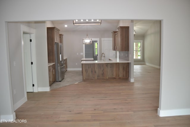 kitchen with backsplash, kitchen peninsula, pendant lighting, high end fridge, and light wood-type flooring