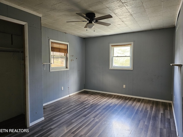 unfurnished bedroom with ceiling fan, a closet, dark wood-type flooring, and wooden walls