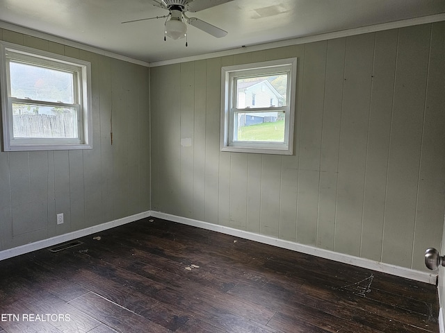 empty room featuring wood walls, ceiling fan, ornamental molding, and dark hardwood / wood-style floors