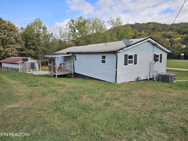 rear view of property featuring central AC unit, a wooden deck, and a lawn