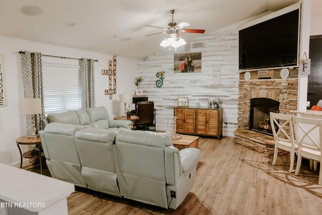 living room with light hardwood / wood-style flooring, a stone fireplace, vaulted ceiling, and ceiling fan